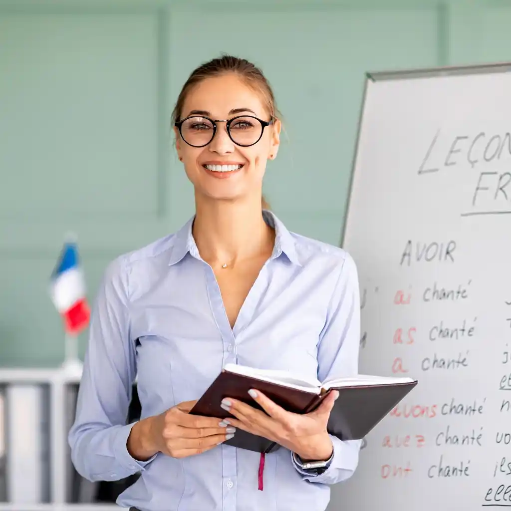 Une professeure de français Scol'Avenir de Moyeuvre se tient devant un tableau en souriant, avec des livres en main
