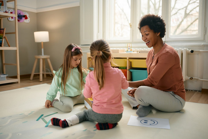 Fille au pair heureuse jouant et dessinant avec deux petites filles