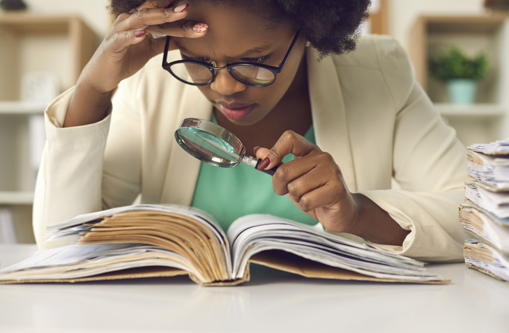 Jeune lycéenne avec des lunettes regardant un texte à la loupe pour en faire une analyse