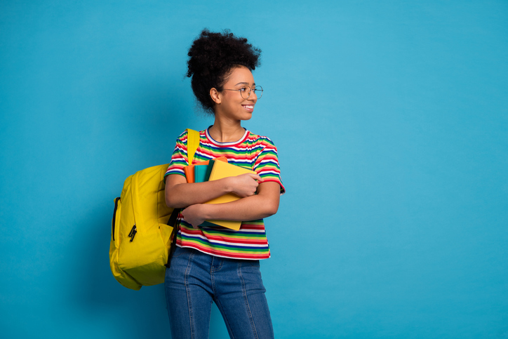 Lycéenne avec un sac à dos jaune contenant un livre, portant un t-shirt rayé coloré et des cahiers de SES