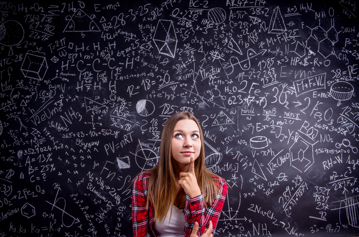 Etudiante de première au lycée à Thionville en chemise à carreaux rouges se tient devant un grand tableau noir couvert de symboles et de formules mathématiques d'équations du second degré.