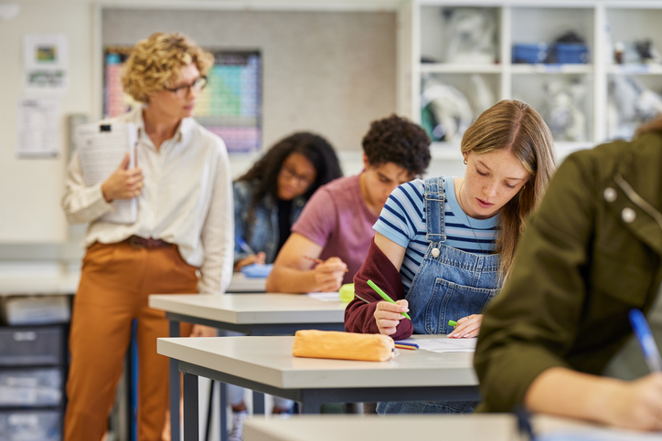 Une enseignante expérimentée surveille des élèves pendant un examen de maths dans une salle de classe d'un lycée. Des garçons et des filles passent leurs examens sous la surveillance de leurs professeurs de première.