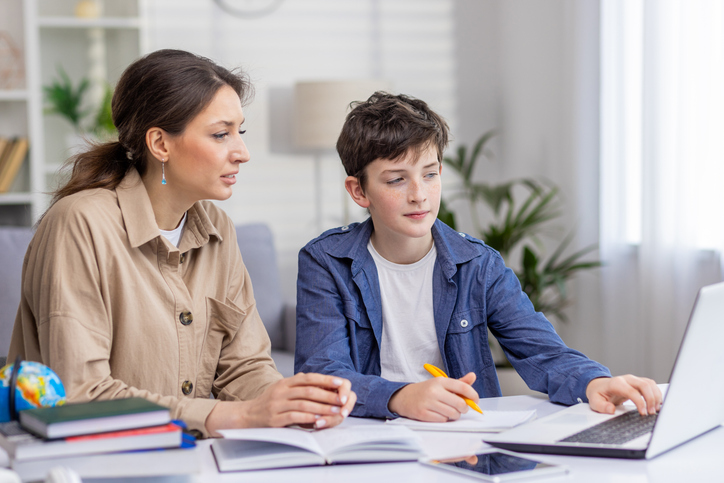 Une mère et son fils étudient ensemble, assis à un bureau dans le salon ; la mère aide son fils à faire ses devoirs de mathématiques à la maison.