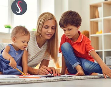 Nounou à domicile qui fait du coloriage avec deux enfants par terre