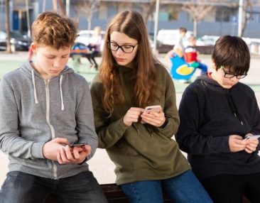 Groupe de trois élèves regardant leur téléphone dans un parc