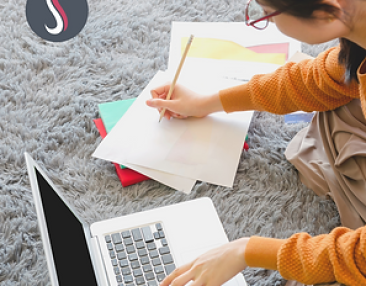 Jeune fille assise écrivant ses leçons sur une feuille et sur un ordinateur