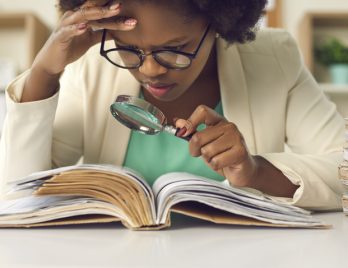 Jeune lycéenne avec des lunettes regardant un texte à la loupe pour en faire une analyse