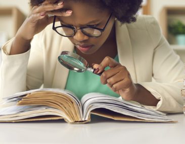 Jeune lycéenne avec des lunettes regardant un texte à la loupe pour en faire une analyse
