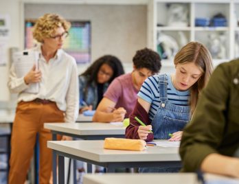Une enseignante expérimentée surveille des élèves pendant un examen de maths dans une salle de classe d'un lycée. Des garçons et des filles passent leurs examens sous la surveillance de leurs professeurs de première.