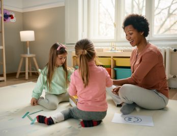 Fille au pair faisant des dessins avec des enfants heureux Fille au pair heureuse jouant et dessinant avec deux petites filles