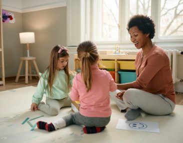 Fille au pair heureuse jouant et dessinant avec deux petites filles