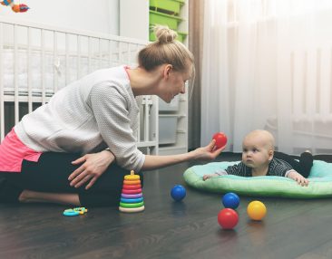 Nourrice qui s'occupe d'un bébé qui est sur un tapis d'éveil