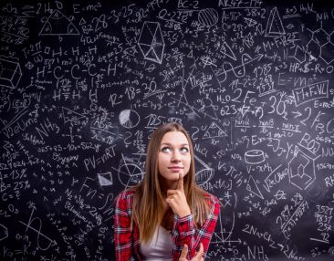 Etudiante de première au lycée à Thionville en chemise à carreaux rouges se tient devant un grand tableau noir couvert de symboles et de formules mathématiques d'équations du second degré.