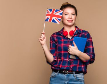 Une étudiante tient un petit drapeau britannique et un cahier dans un studio sur fond beige. Cours particulier d'anglais. Apprentissage de l'anglais britannique.