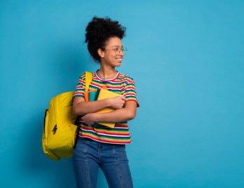 Lycéenne avec un sac à dos jaune contenant un livre, portant un t-shirt rayé coloré et des cahiers de SES